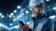 © watcharee - A male engineer in safety gear uses a smartphone in a high-tech industrial setting with bright lights.