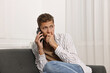© New Africa - Worried man calling hotline for mental health help on sofa at home