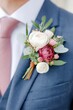 © Natalia - Elegant floral boutonniere featuring white, pink, and deep red blooms, adorned with greenery, attached to a tailored blue suit, enhancing formal attire for special occasions