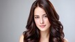 © lililia - Attractive woman with long, wavy brown hair smiles confidently in a studio against a neutral background, highlighting her hair's shine