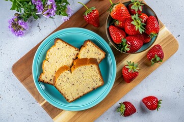 Poster - A blue plate holds sliced bread on a wooden cutting board. Strawberries surround the plate, suggesting a snack or dessert setting.
