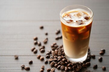 Poster - A glass of iced coffee with ice cubes and coffee beans scattered around it on a wooden surface.