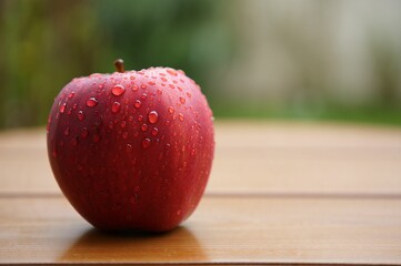 Aufkleber - A red apple with droplets of water on it, sitting on a wooden surface.