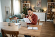 © Migma_Agency - Focused freelancer reading documents and working on laptop at home