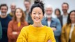 © Pris - Smiling Asian woman wearing a yellow sweater with people standing behind her. Diversity and inclusion within a community is obvious.