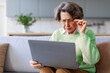 © Home-stock - Poor eyesight. Senior woman using laptop, touching glasses and squinting eyes, having problems with vision, sitting on sofa at home, copy space
