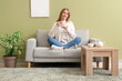 © Pixel-Shot - Young woman with cup of tea sitting on sofa at home