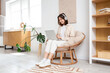 © Pixel-Shot - Young woman with headphones using laptop in cocoon chair at home