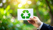 © emwe studio - Green future: Hand holding recycling symbol amidst vibrant nature background