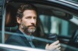 © Marius - Professional man commuting in hybrid car while holding reusable coffee cup during morning routine in urban setting