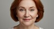 © irissca - Woman with short red hair smiling gently against a neutral background showcasing warm expression and confidence