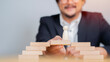 © Kunlathida - Happy businessman making a bridge of wooden blocks for people wooden icon to walk across