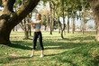 © saltdium - An active young woman stretches her arms outdoors in a sunny, green park surrounded by nature and fresh air