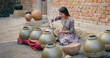 © Raushan_films - Indian teenage village woman wear casual dress sitting outdoor making hand made potters finishing touches clay pots asian young female learning handcraft create sculptor pottery mud product outside