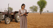 © Raushan_films - Indian young adult village woman wear casual dress tablet tab gadget do online work check field area data farmer teen age girl lady use device screen outside desi life