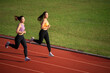 © WARAPHON - Two women running on a track. One is wearing a pink top and the other is wearing an orange top