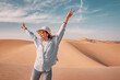 © EdNurg - Happy female tourist raising her arms in joy, reveling in the warmth of the sun and the stunning desert landscape around her