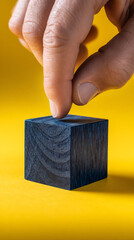 Poster - Close-up of fingertip touching dark-blue wooden cube on yellow background, showcasing minimal product display concept, ideal for branding or advertisement