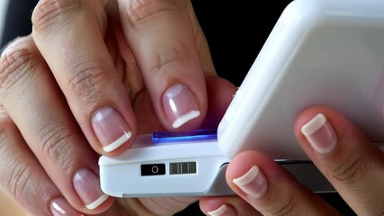 Poster - Close-up of female hands using a white electronic device with a glowing blue UV light strip