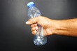 © The Prince  - hand holding a used water bottle crushing by hand on dark background closeup view
