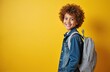 © Maryna - Happy schoolboy with curly hair, backpack smiling against yellow background. Portrait of smiling student, back to school concept. Education, childhood joy, elementary school.