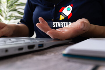 Poster - Woman working on laptop holding a rocket icon and the word Startup