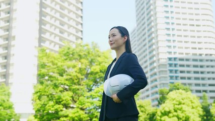 Aufkleber - 新緑の街の前にヘルメットを持って立つ女性ビジネスパーソン