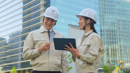 Poster - 建設現場でタブレットを見ながら打ち合わせする男女エンジニアのグループ