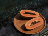 Sliced papaya on a wooden plate by the pool. Tropical fruit in natural sunlight, creating a relaxing and healthy summer vibe.