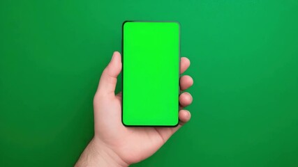 Poster - Hand holding smartphone with green screen on vibrant green background for creative applications and design use