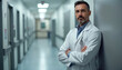 © Vadym - Confident doctor with crossed arms stands in hospital corridor. Professional male physician wearing lab coat looks at camera. Healthcare worker, medical specialist provides patient treatment. Modern