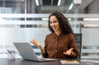 © Liubomir - A businesswoman happily engaged in a video call, gesturing while sitting at her office desk. The laptop, notebook and tablet are on the table.
