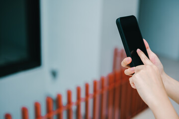 Poster - Smartphone concept. Close-Up of Hands Holding a Smartphone with a Blank Screen in an Outdoor Setting Near a Red Fence