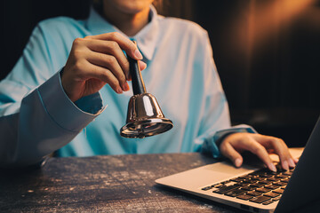 Poster - businessman working. Person Holding Bell While Working on Laptop in Cozy Indoor Environment with Warm Lighting