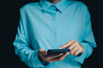 Poster - Smartphone concept. Person Using Smartphone in Dark Environment, Wearing Light Blue Shirt, Focus on Hands and Device