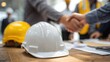 © CStock - Construction professionals shake hands over project agreements while hard hats rest on the table in an office.