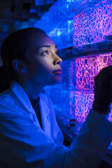 Poster - Woman in lab coat examining glowing cell structures in a brightly lit laboratory setting closely