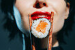 © VICHIZH - Close-up of a female model with red lips holding sushi with chopsticks, featuring a glamorous look and a vibrant color palette.