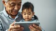 © muhammad azka - An elderly man holds a tablet, sharing content with a young child, both focused intently