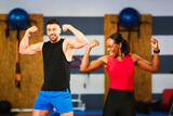 Smiling fit man and woman flexing biceps in gym, expressing strength and healthy lifestyle