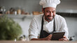 © SolaruS - Happy chef in uniform using a tablet. Depicts modern culinary practices, recipe inspiration, food tech. Ideal for culinary blogs, restaurant promotions.