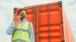 © VAKSMANV - Portrait busy professional supervisor of freight transportation company talking on phone wearing safety glasses and helmet. African hard-working worker standing in front of red container communicating