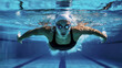 © Ella - Athletic woman swims underwater in a pool, wearing a black swimsuit, swim cap, and goggles. The light reflections on the water enhance the sense of motion and intensity of the sport.