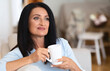 © Prostock-studio - Weekend Leisure. Portrait of smiling mature woman drinking hot coffee, holding cup and sitting on the couch in living room. Happy lady enjoying good morning. Resting And Relax Concept