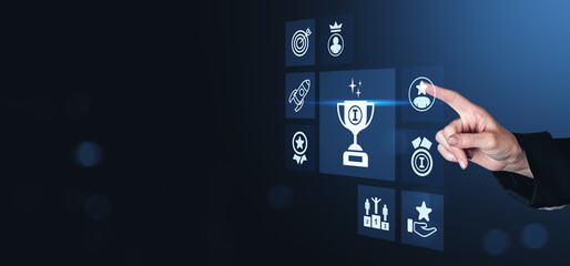Poster - Business hand pointing at digital icons of trophy, awards, and success symbols on futuristic blue interface screen representing achievement concept.