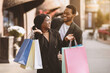 © Prostock-studio - Fun and shopping together on black friday and final sale. Happy african american young guy and lady in coats enjoying walk, look at each other and hold many colorful bags with purchase, copy space