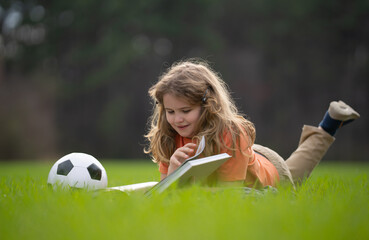 Aufkleber - Kid read a book in the grass. Kid read a book story outdoors. Kid read book in the meadow on a sunny day. Reading in nature. Schoolboy with book. Kid outdoor learning. Kids read story.