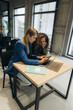 © Roman - Two Women Collaborating on a Project Using a Laptop and Smartphone