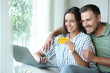 © Antonioguillem - Happy couple buying online using card and laptop in a house