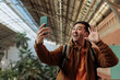 © bernardbodo - Young man video calling and waving in train station